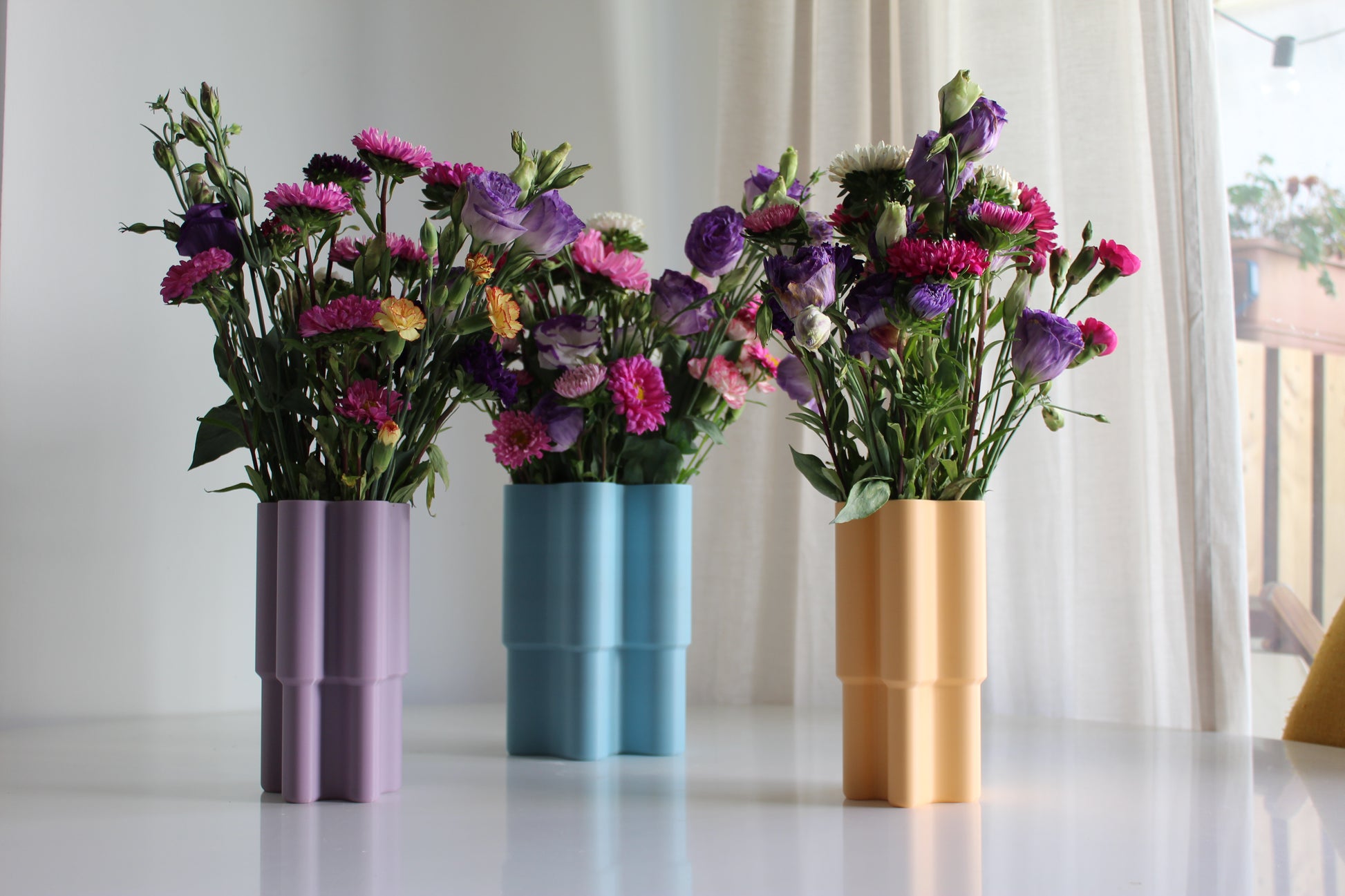 3 mini vase violet, bleu et orange mis en scene sur une table de salle à manger, pastel design, objet déco, fleurs colorés, impression 3D, artisanat francais, écoresponsable, slow design, matériau végétal recyclé